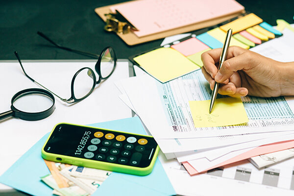 person writing on a sticky note while reviewing documents