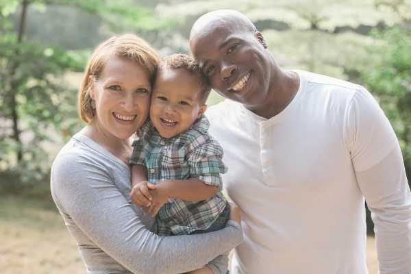 mother, father, and baby smiling surrounded by trees